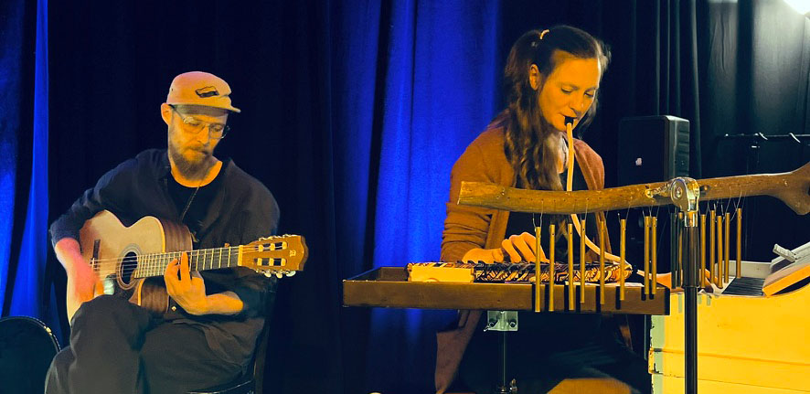Boomcoustix performen akustisch Reggae und Ska. Auf dem Bild sind Eduard an der Akustikgitarre und Jasmin an Melodika und Klavier bei einem Live-Auftritt abgebildet.